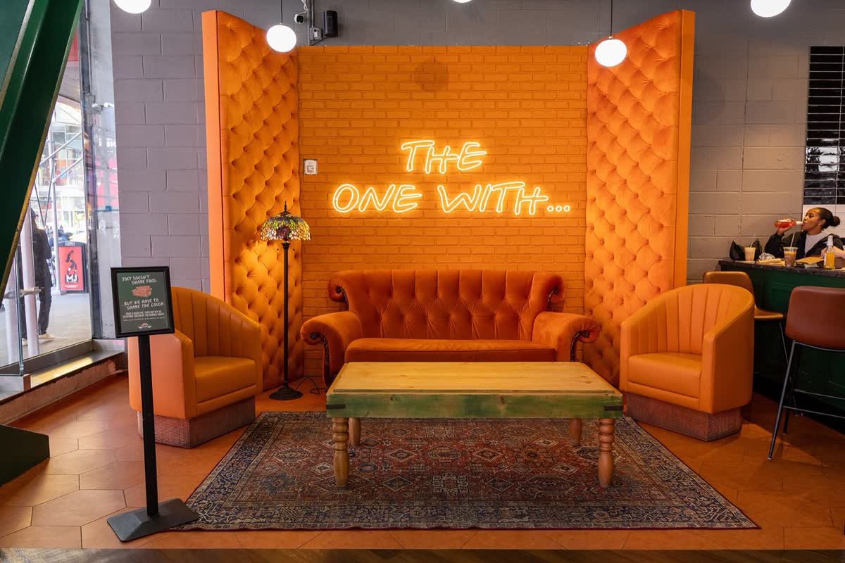 An orange couch and armchairs under a neon sign